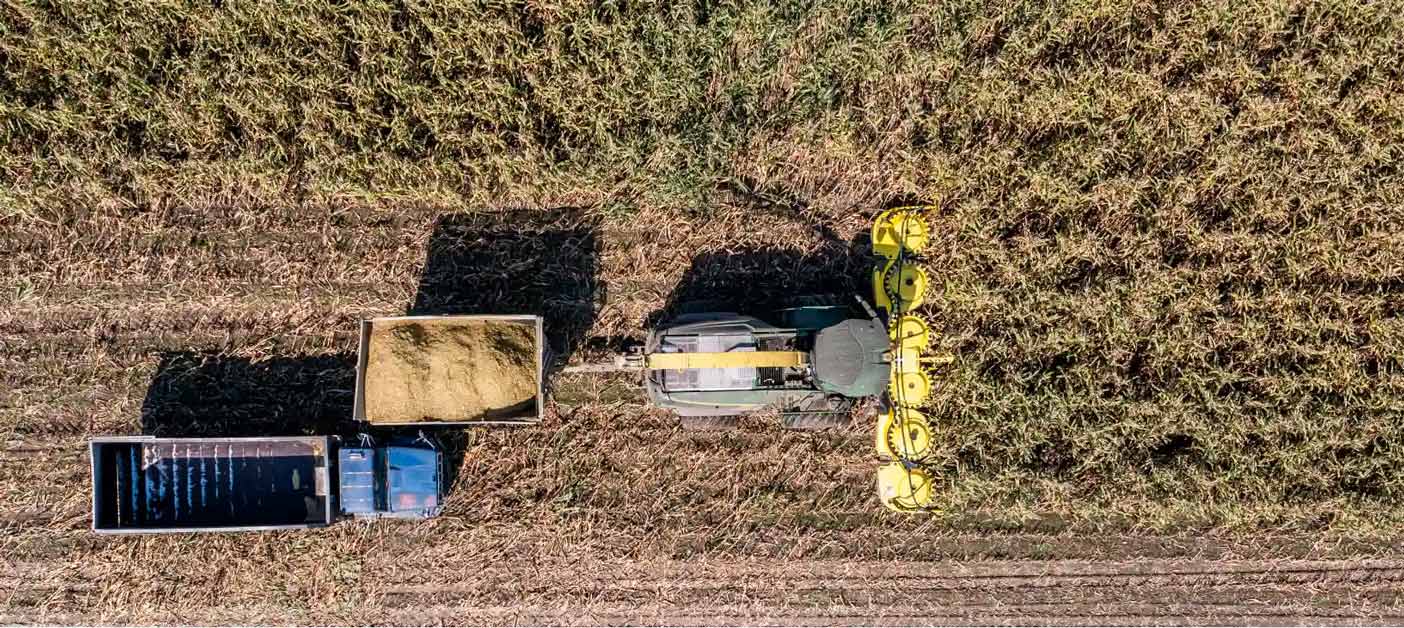 An aerial view of a Combine machine harvesting corn in a large field.
