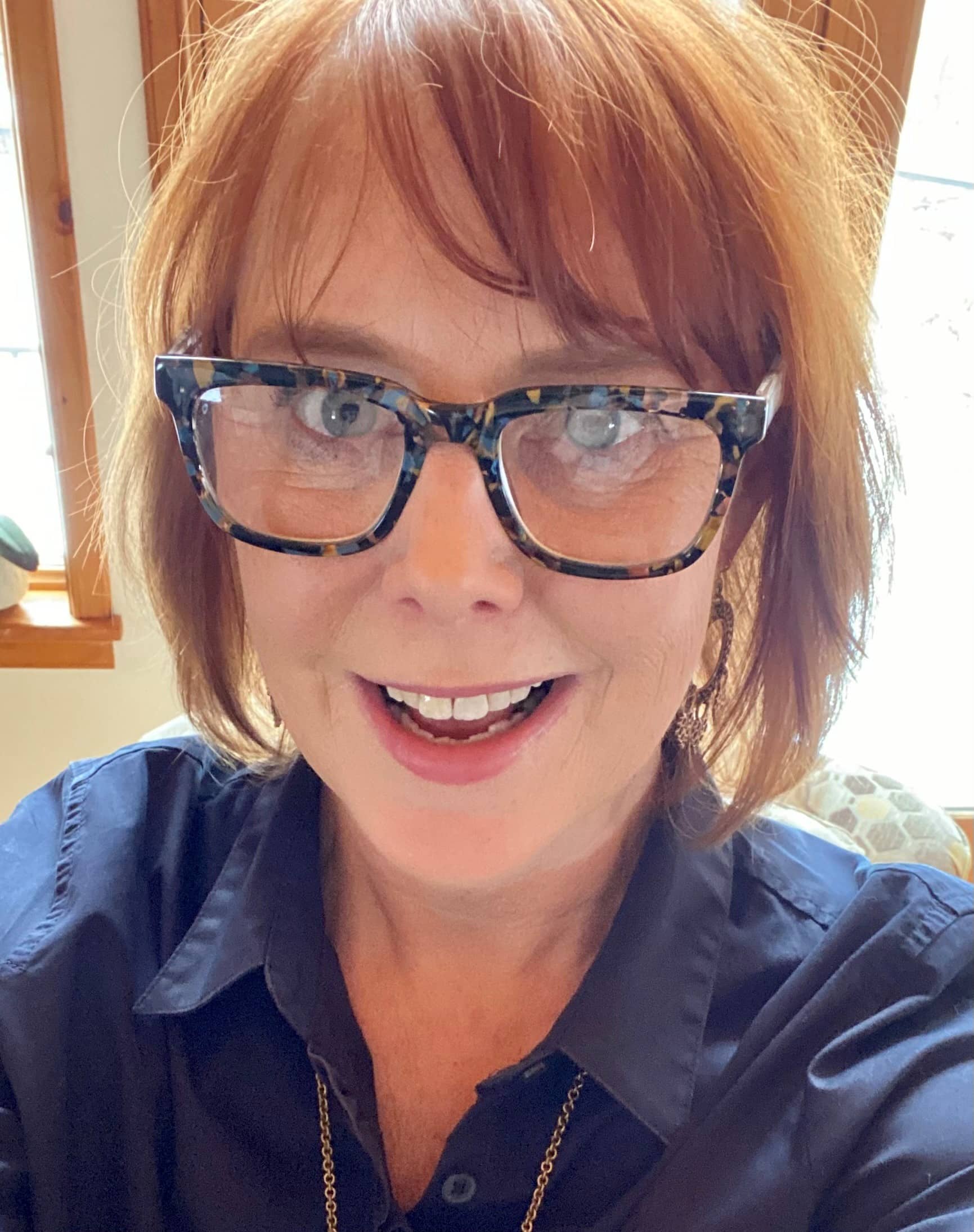 Ann Nygard, a woman with red hair and rectangular glasses, smiling at the camera.