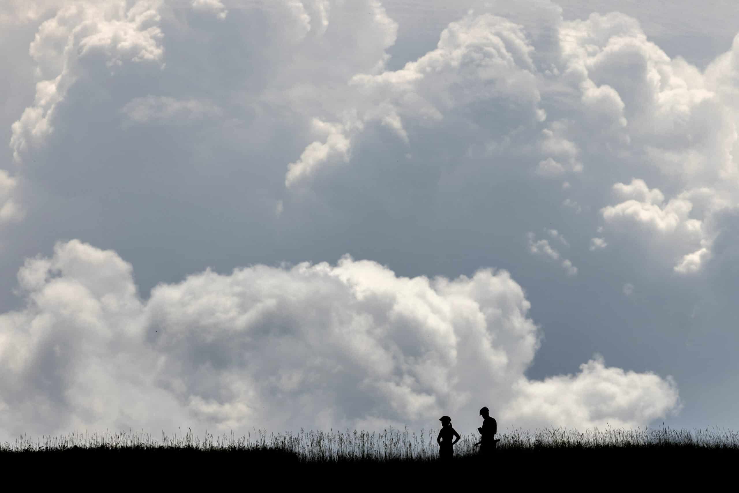 Two people riding bikes through a field silhouetted against billowing clouds