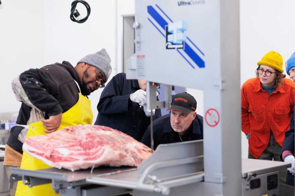 A man running a large piece of raw meat through a saw